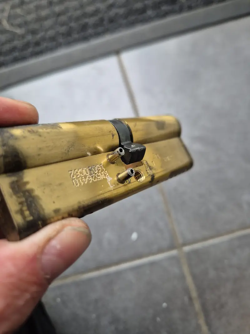 Brass-coloured cylinder held in a hand, with its centre cam and two metal fittings visible